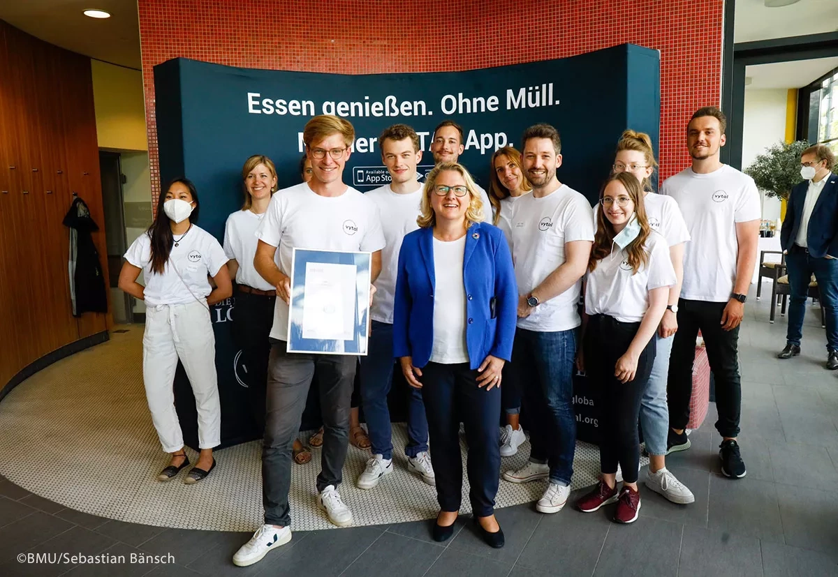 Junge Menschen lachen zusammen mit Frau Schulze und zeigen die Urkunde