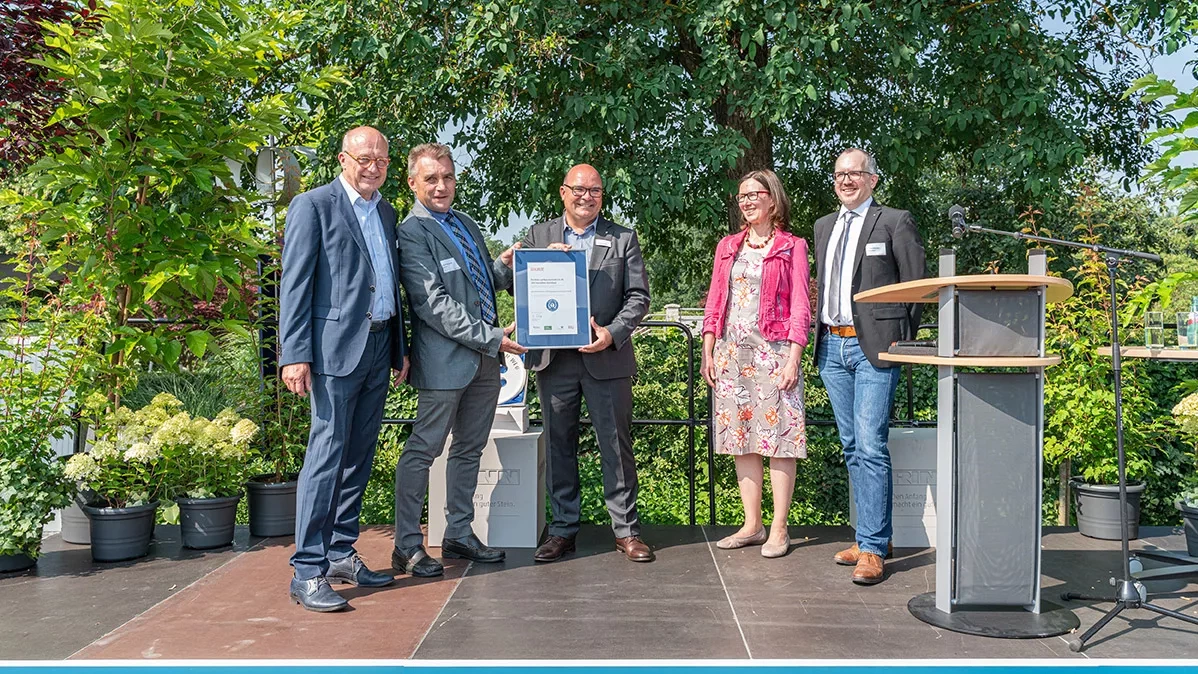 Four men and a woman hold a certificate up to the camera. Underneath is the slogan: RINN, A good stone makes the beginning.