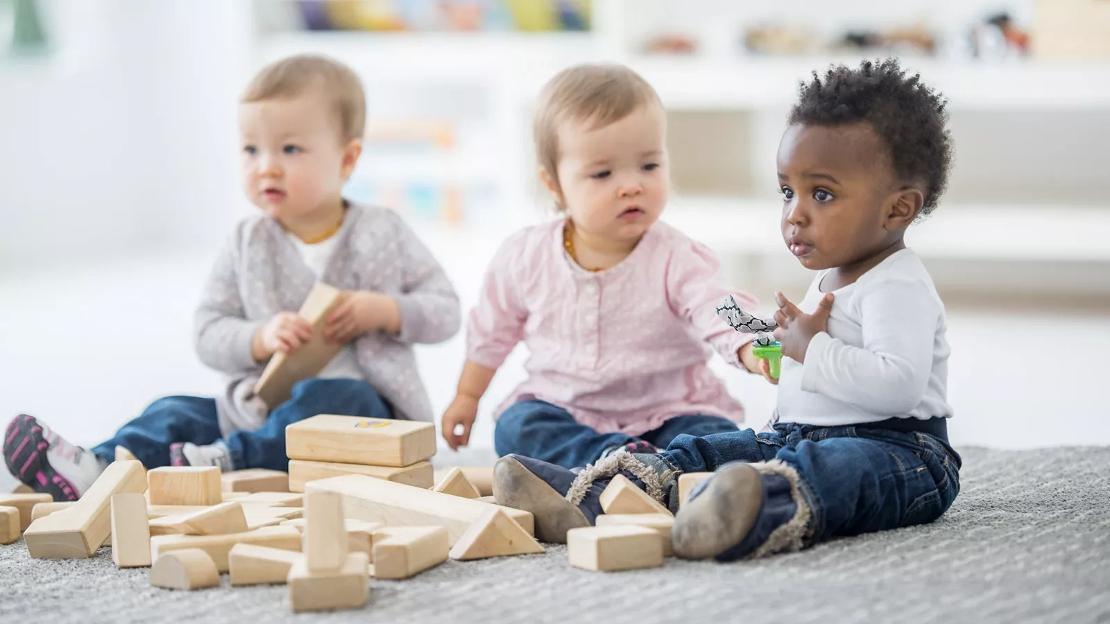 Drei Kleinkinder spielen mit naturbelassenen Bauklötzen