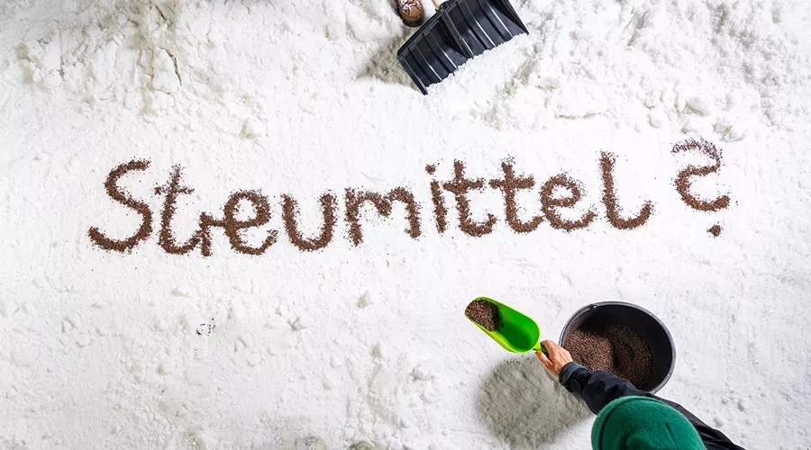 Wort Streumittel mit Kieselsteinen im Schnee