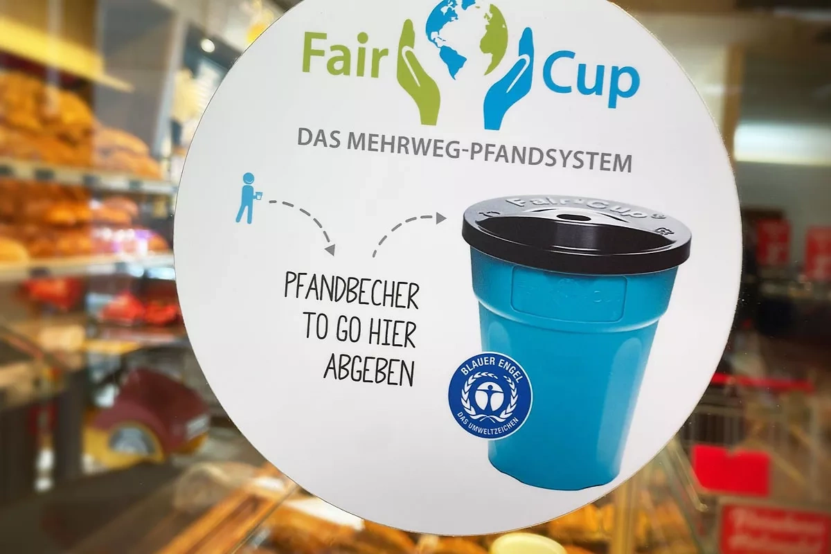 Schild an einem Lebensmittelladen: FairCup. Das Mehrweg-Pfandsystem. 