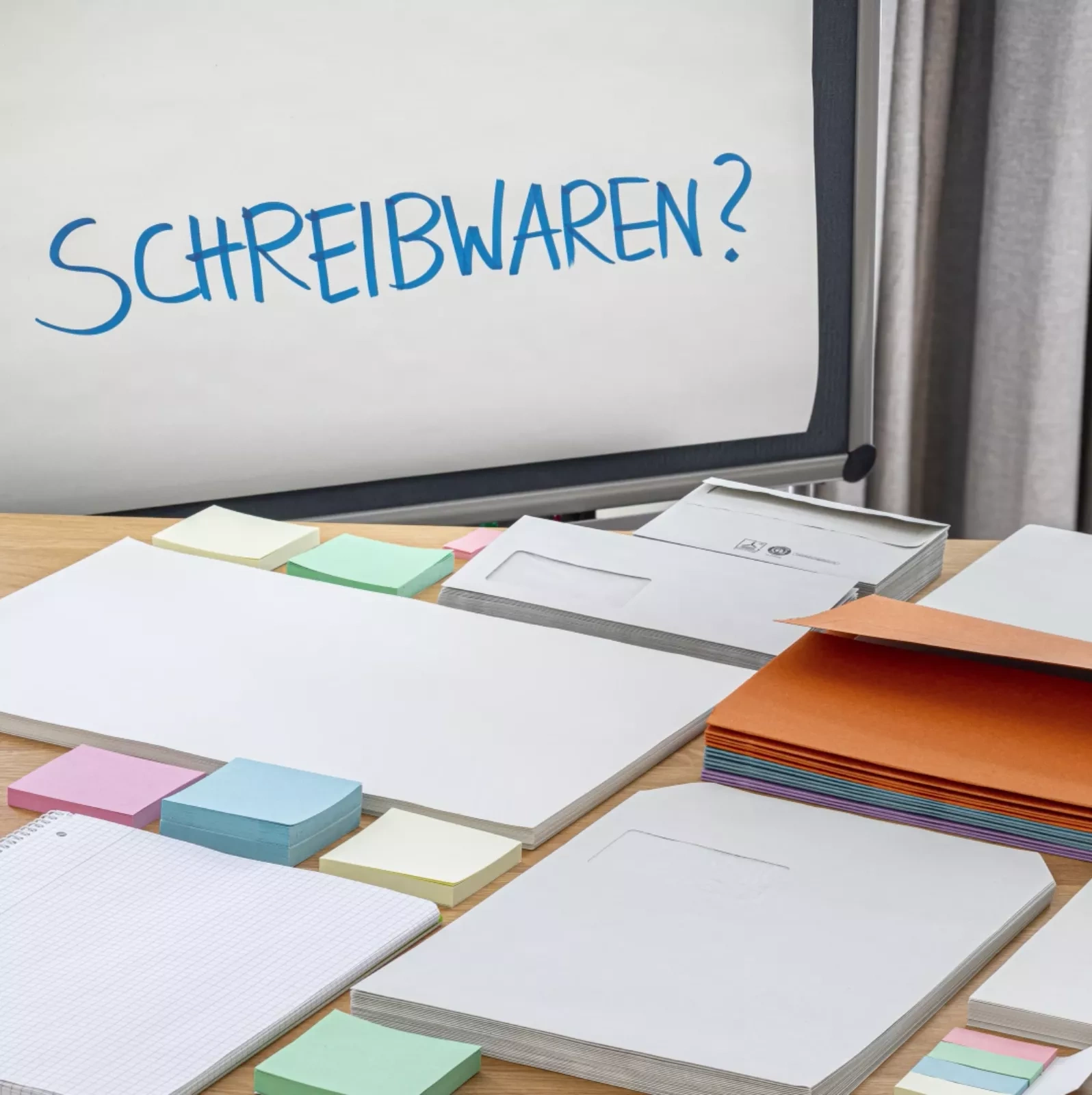 Schreibwaren? steht auf einem Plipchart und davor auf einem Tisch liegen viele verschiedenen Papierprodukte wie Stick Notes, Briefumschläge, Aktenmappen und Co.