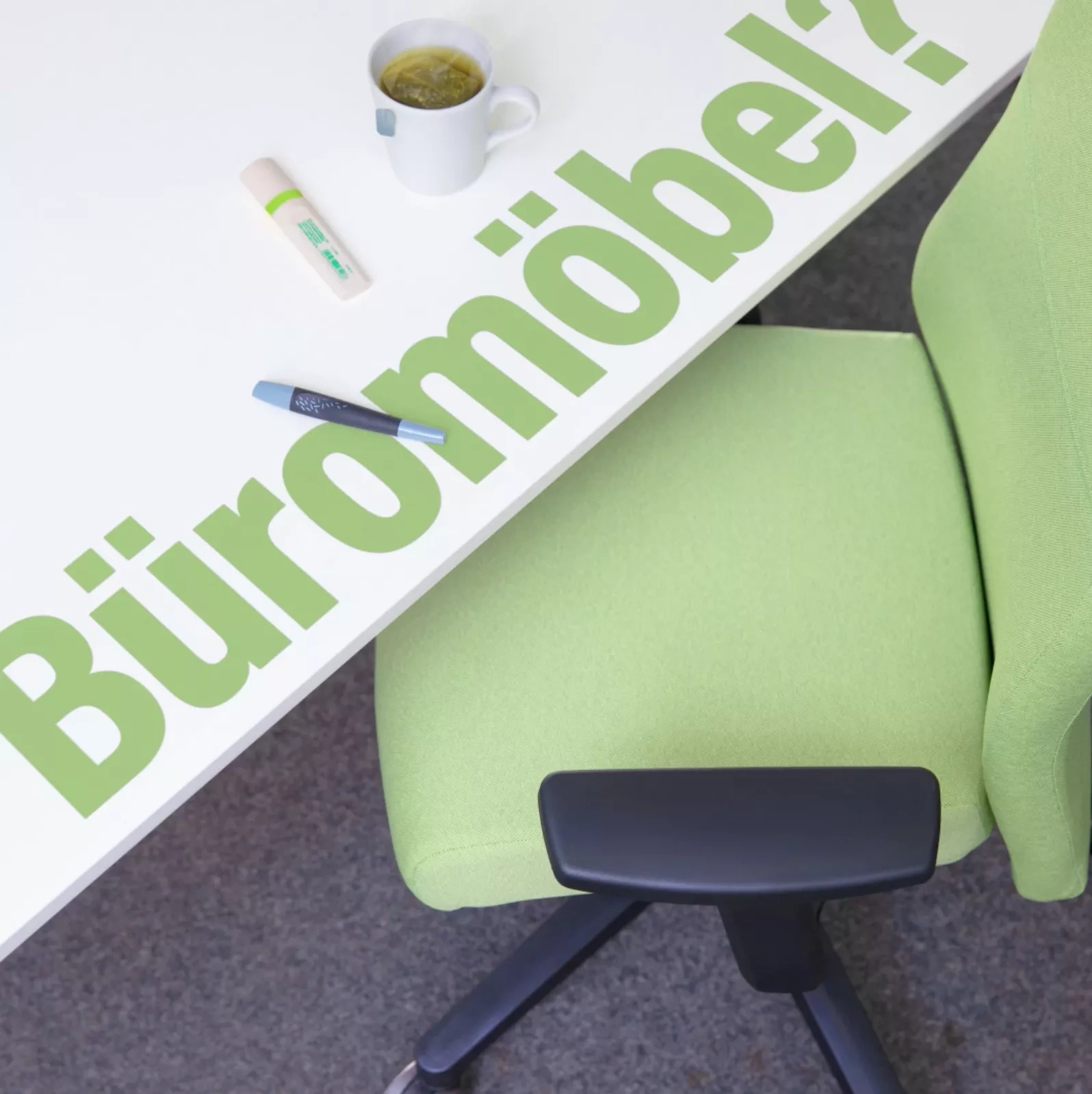 Büromöbel? - umweltschonend! Ein hellgrüner Bürostuhl steht an eine weißen Schreibtisch auf dem zwei Stifte liegen und eine Tasse Tee steht.