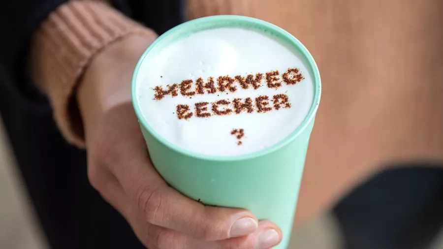 Becher mit Cappuccino und geschrieben das Wort Mehrwegbecher mit Kakaopulver