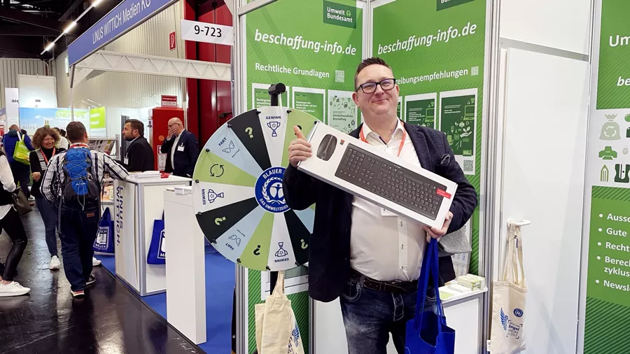 Ein Mann hält eine Verpackung mit Tastatur vor dem Messestand des Umweltbundesamtes hoch 