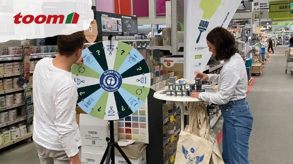 A man spinning the wheel of fortune and a woman at a bar table in the DIY store, with the toom logo on the left.