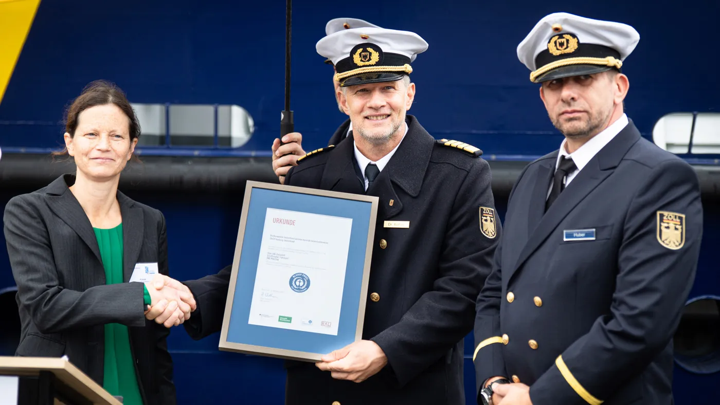 Frau und drei Männer in Zolluniformen, Ein Mann hält die Urkunde in der Hand. 