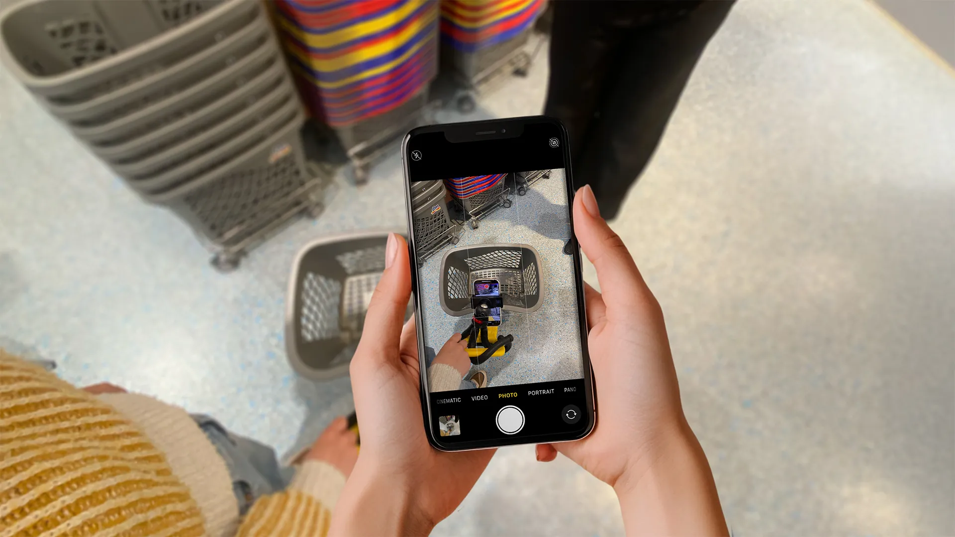 Zwei Hände halten ein Smartphone im Kameramodus auf einen Einkaufskorb