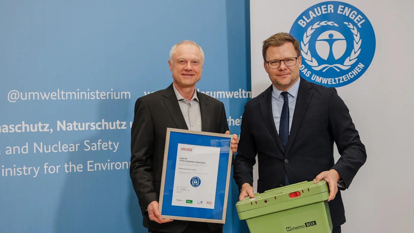 Person hält die eingerahmte Urkunde und daneben steht Bundesumweltminister Schneider mit einer Mehrwegbox von memo