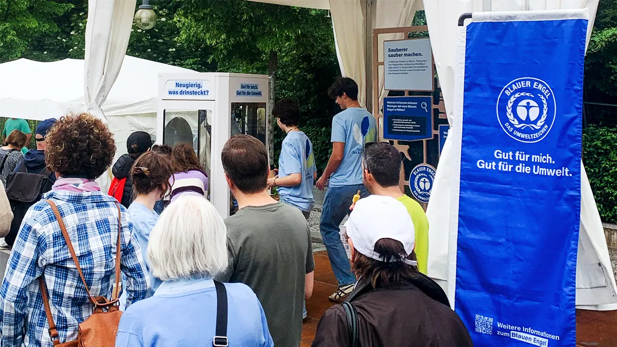 Menschen blicken Richtung eines Stands vom Blauen Engel