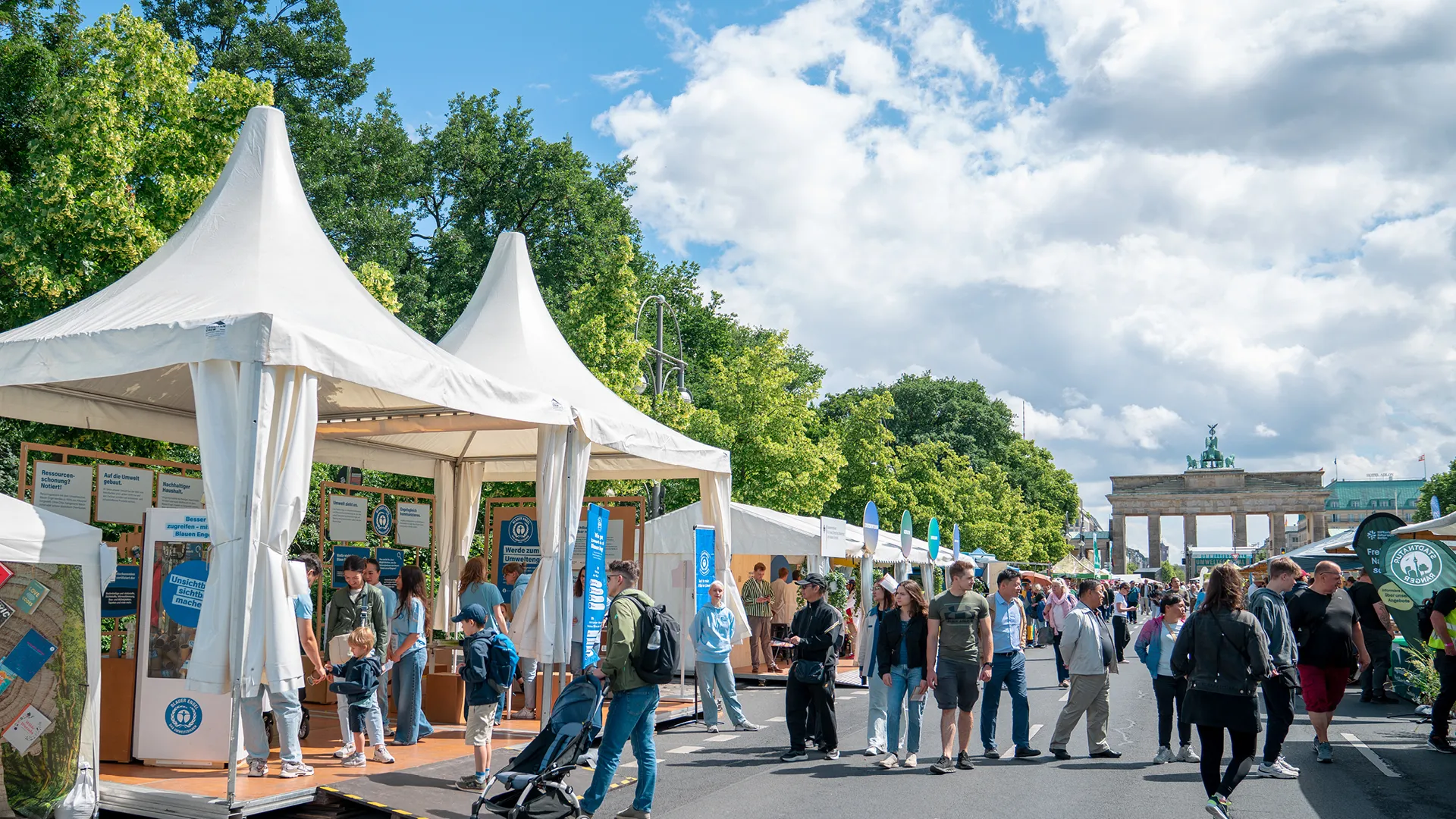 Blauer Engel Stand draussen im Sommer mit Menschen und weissen, offenen Zelten, Veranstaltungsrueckblick